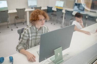 Bilgi işlem dersi. Kızıl okul çocuğu bilgisayar sınıfında bilgisayar üzerinde çalışıyor.