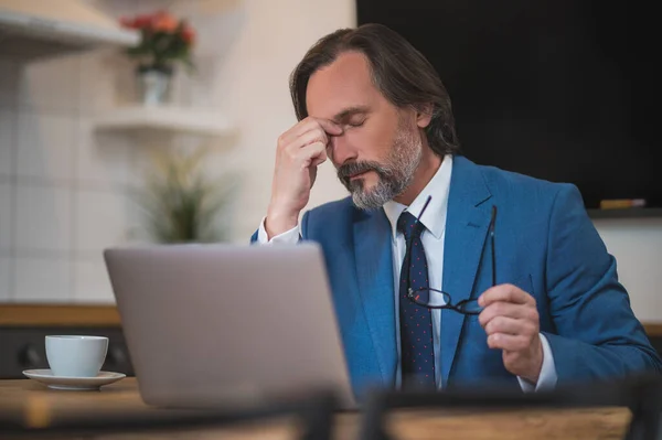 Lots of work. Mature businessman sitting at the laptop and looking tired