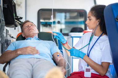 Ambulans doktoru steteskopla kalp atışlarını dinlerken sedyede yatan hasta adam.