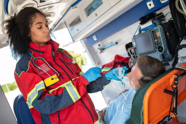 戴着氮肥手套的严重女性辅助医务人员把氧气面罩戴在救护车上的男人身上 — 图库照片