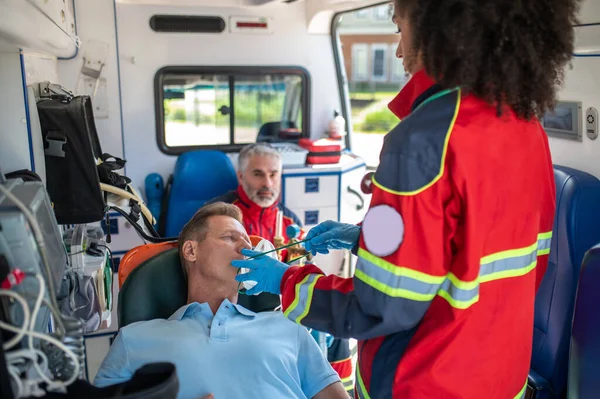 女性辅助医务人员在一位男性同事在场的情况下将氧气面罩戴在一位不省人事的病人身上 — 图库照片