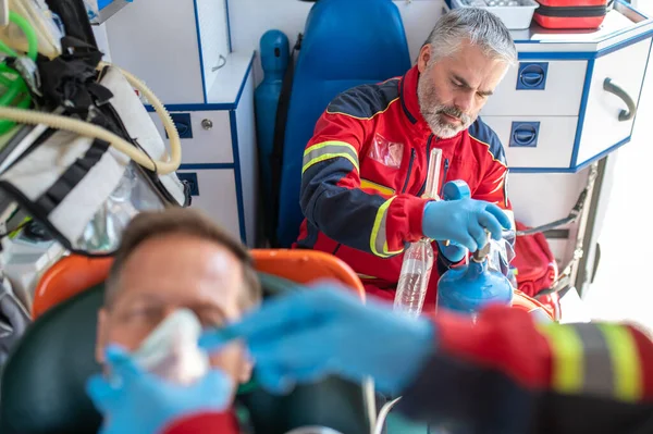 Paramedic opening the valve opening the breathing apparatus valve while his colleague putting the oxygen mask on the patient