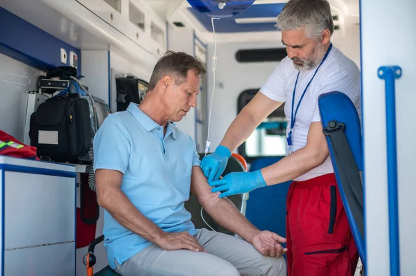 病人坐在救护车车厢里 一名辅助医务人员将导管插入他的静脉 — 图库照片