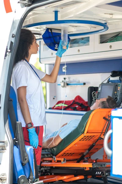 救护人员将盐水瓶悬吊在救护车车顶上 盖住躺在担架上的病人 — 图库照片