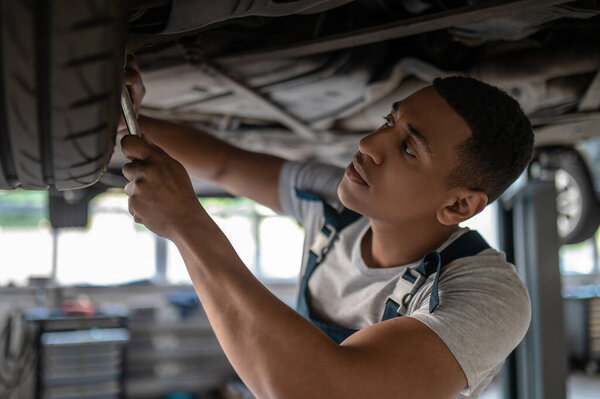 Serious focused African American mechanic tightening the nuts on the automobile wheel with a wrench