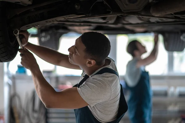 Mechanic tightening the bolts on the automobile wheel with a wrench assisted by his colleague