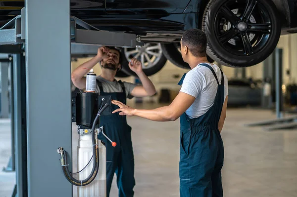 Team Automotive Service Workers Work Clothes Examining Underside Jacked Automobile — Stock Photo, Image