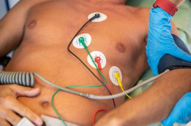 Göğüs kafesinde elektrotları olan hasta sırt üstü yatarken doktor kan basıncını koluna takıyor.
