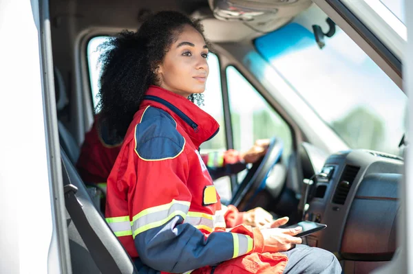 Female doctor with the tablet computer sitting beside the driver in the medical emergency vehicle and looking into the distance