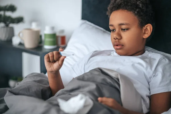 病気の少年は熱でベッドに横たわって温度をチェック — ストック写真