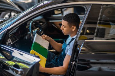 Müşteri arabasının kabininde oturan tamirci, motor hava filtresini kutudan çıkarıyor.