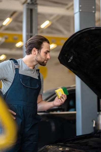 Serious concentrated vehicle mechanic with the automotive part box looking under the open car hood