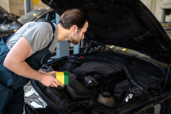 Professional mechanic holding the auto part box in his hands and leaning over the open vehicle hood