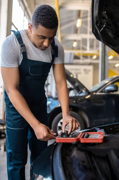 African American auto mechanic in work clothes taking a magnifier out of the open toolbox