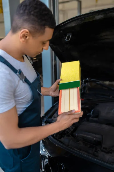 作業服のアフリカ系アメリカ人自動車技術者が新しい車の空気フィルターを箱から取り出し — ストック写真