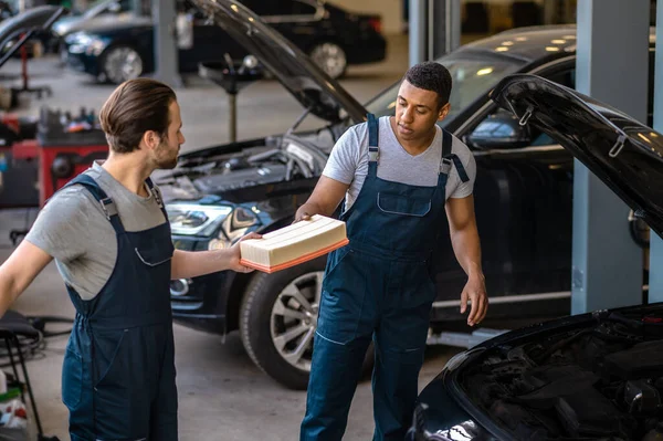 Experienced car repair shop workers in work clothes changing the air filter the customer vehicle