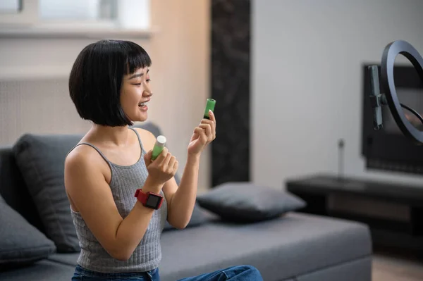 Uśmiechnięty Bloger Wideo Siedzący Przed Kamerą Smartfona Trzymającą Kosmetyki Rękach — Zdjęcie stockowe
