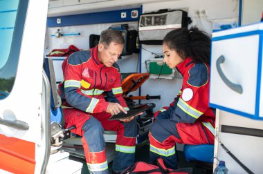 Ambulans arabasında ciddi bir bayan arkadaşının önünde tablet bilgisayarı kullanan konsantre bir sağlık görevlisi.