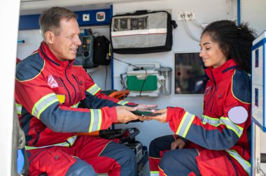Gülümseyen doktor tableti ambulans arabasındaki memnun bayan arkadaşına veriyor.