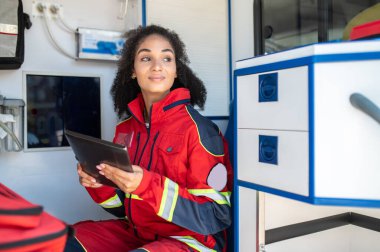 Gülümseyen kadın doktor ambulans arabasında otururken elinde tablet bir bilgisayar tutuyor.