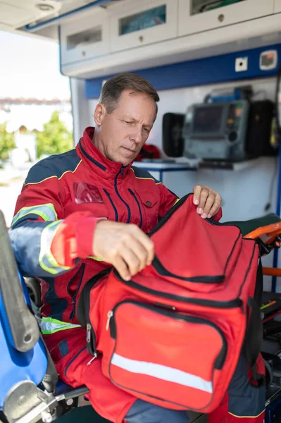 Médico Concentrado Uniforme Rojo Sentado Coche Ambulancia Mientras Abre Bolsa — Foto de Stock