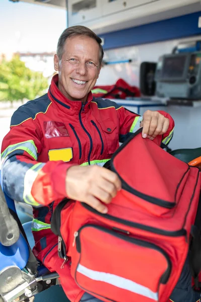 Profesional Paramédico Alegre Uniforme Rojo Sentado Coche Ambulancia Abriendo Bolsa — Foto de Stock