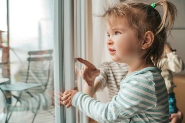 Güzel, sarı saçlı, at kuyruklu bir çocuk. Annesinin uzaktan izlediği bir şeye bakıyor.