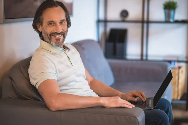 Work from home. Good-looking mature man sitting on a sofa with a laptop