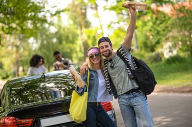 İyi hissediyorum. Sevimli genç çift arabanın yanında heyecanlı ve neşeli duruyor.