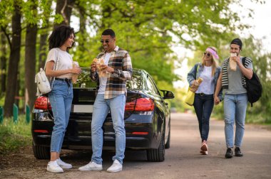 Ormanda öğle yemeği. Bir grup arkadaş ormanda arabanın yanında durup yemek yiyor ve bir şeyler tartışıyorlar.