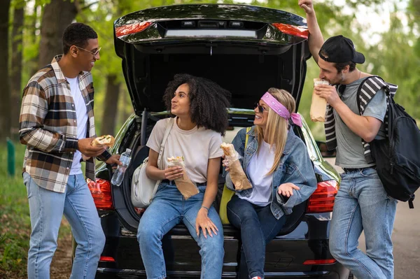 Lunch in the forest. Group of riends having lunch and discussing something while standing near the car in the forest