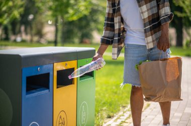 Geri dönüşüm için. Genç Afrikalı Amerikalı adam çöp kutusuna plastik şişe atıyor.