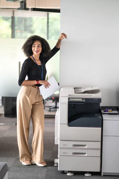 Confident woman. Confident good-looking young woman standing near xerox in the office