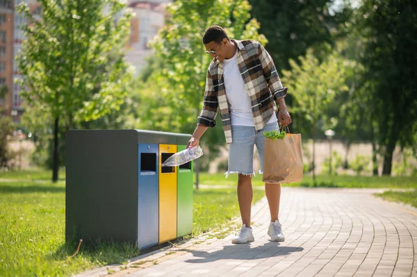 Geri dönüşüm için. Genç Afrikalı Amerikalı adam çöp kutusuna plastik şişe atıyor.