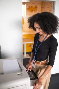 Belgeler. Koyu saçlı, iyi giyimli, fotokopi çeken bir kadın.