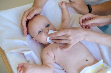 Burun temizleme. Doktorlar muayene ederken annem peçeteyle bebeklerin burnunu temizliyor.