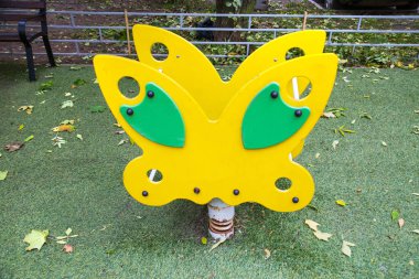 Güneşli bir günde, tahta bir kelebek şeklinde metal bir yay üzerinde sallanan sandalye. Oyun alanları, spor, sağlık eğlencesi.