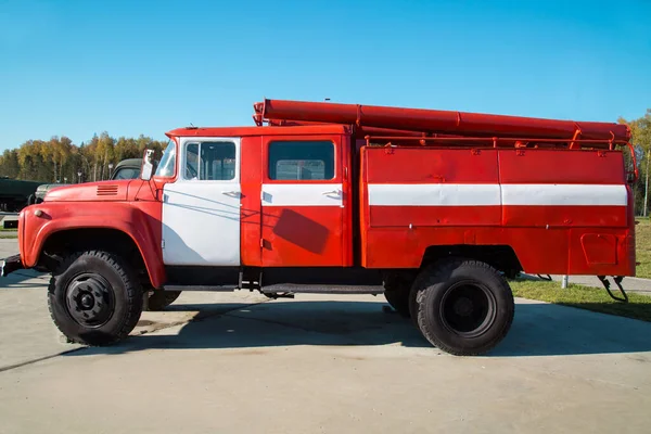 Mavi arka planda beyaz çizgili kırmızı bir itfaiye aracı açık güneşli bir günde askeri teçhizat atom uçakları helikopterleri.