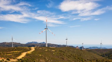 Sardunya 'daki bir dağ rüzgâr çiftliğinde bulutları olan güzel mavi gökyüzünde rüzgar türbinleri. Yenilenebilir enerji konsepti, yeşil enerji üretimi. Enerji endüstrisi.