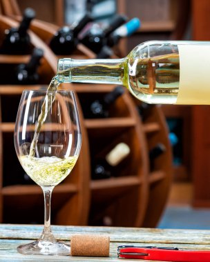 Şaraphane. Kırsal bir ahşap masada şarap tatmak için şişeden şarap kadehine beyaz şarap dökmek. İçecek, alkol..