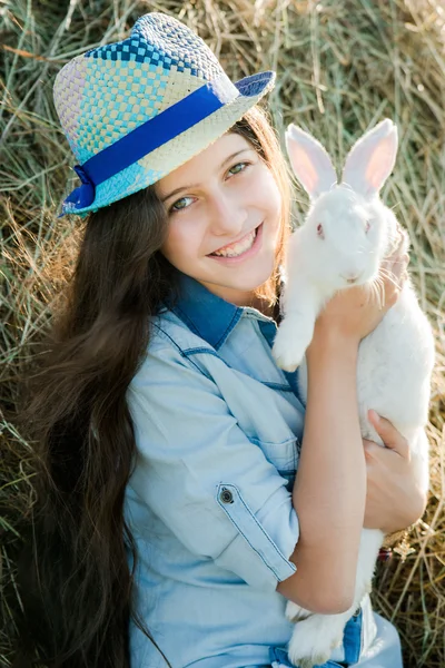 Cute teen girl with white rabbit sitting in front of haystack — Stock Photo, Image