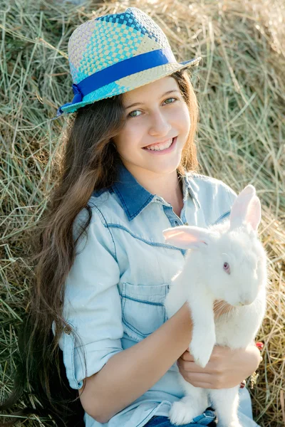 Süßes Teenie-Mädchen mit weißem Kaninchen sitzt vor Heuhaufen — Stockfoto