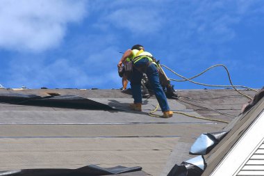 Roofers are attempting to lay a base of tar paper on a roof before the permanent shingles are fastened. clipart