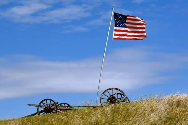 草の丘に木製の車輪を持つ古いワゴントレーラーは 米国の国旗をサポートしています — ストック写真