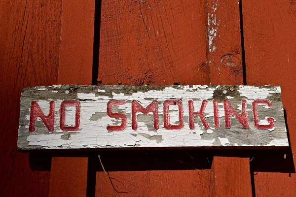 An old weathered and worn NO SMOKING sign is attached to an equally old red door.