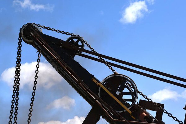 The cables and wheels of a steam powered bucket are silhouetted against the blue sky.