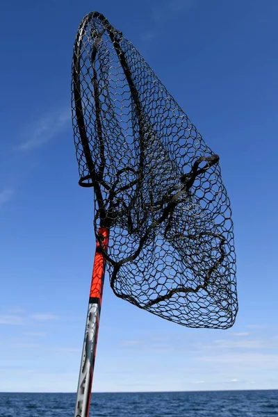 A black net used land fish in a boat is standing upright in a boat and blowing in the wind.