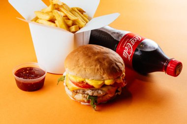 Sarı arka planda çizburger, patates kızartması, kola ve ketçap.