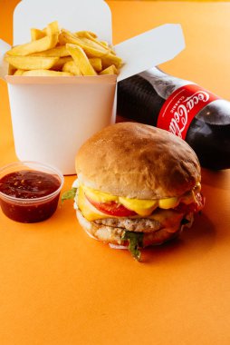 Sarı arka planda çizburger, patates kızartması, kola ve ketçap.