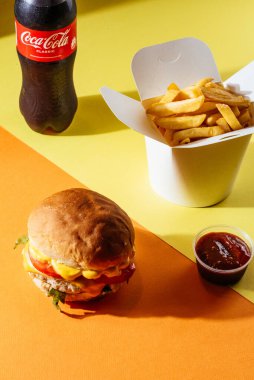 Sarı arka planda çizburger, patates kızartması, kola ve ketçap.
